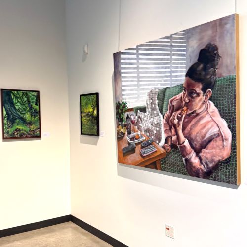 Works by Kathy Frugé Brown and Robin Arnitz Corner of art gallery with two small tree landscapes and a large painting of a woman eating